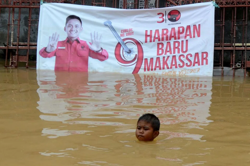 CABARAN DAN HARAPAN: Seorang budak lelaki berenang di kawasan kediaman berikutan banjir di Makassar, Sulawesi Selatan, Indonesia, dengan berlatar belakang sepanduk 'Harapan baru Makassar'. - Foto REUTERS