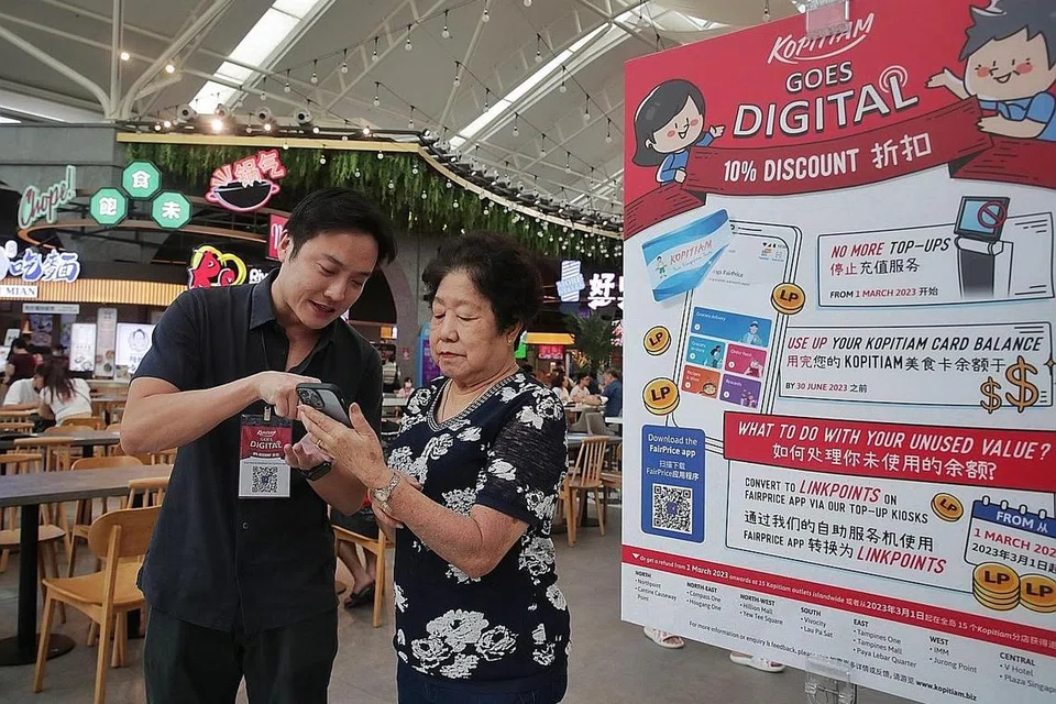 MUDAHKAN PELANGGAN: Seorang rakan digital di cawangan Kopitiam di Jurong Point, Encik Keith Lee, membantu warga emas seperti Cik Peh Ah Eng beralih daripada penggunaan kad fizikal Kopitiam kepada aplikasi FairPrice. - Foto ST