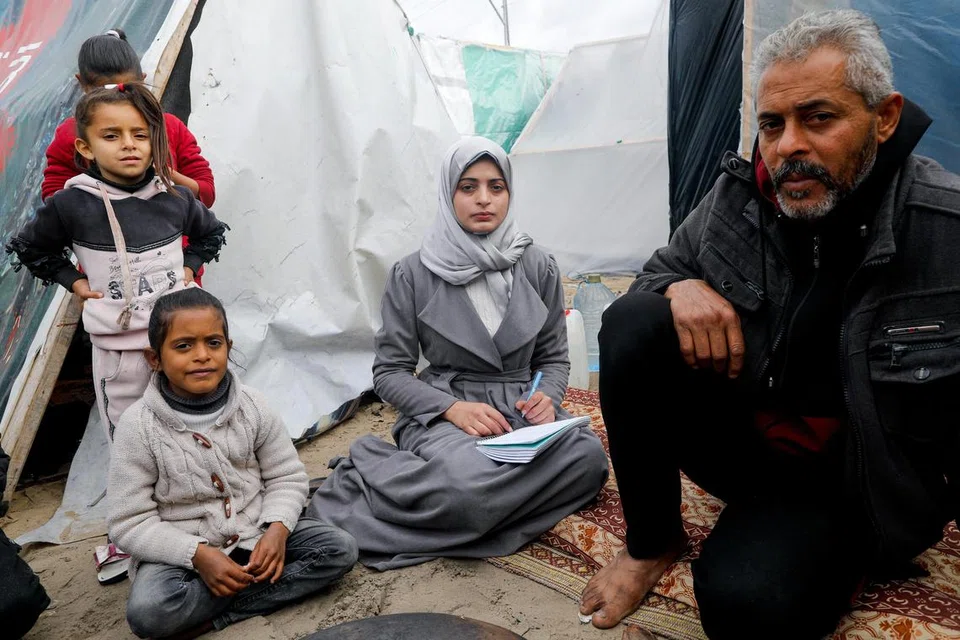 Cik Aseel Abu Haddaf (tengah), pelajar perubatan yang melarikan diri dari rumahnya di Khan Younis bersama keluarganya akibat serangan Israel, duduk di sebelah bapanya di khemah perlindungan, di Rafah, di selatan Jaluran Gaza pada 28 Januari.