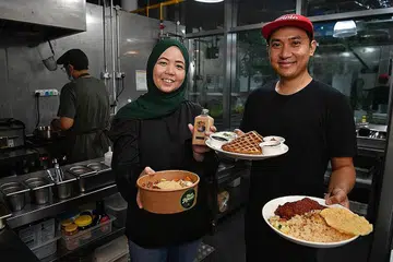 LEBIH KUKUH BERSAMA: Pengasas bersama KloudKitchen Cik Nana Adam dan Encik Dzulkifli Ahmad menunjukkan beberapa hidangan yang disediakan oleh peniaga di sana. - Foto BH oleh CHONG JUN LIANG