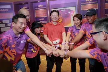 Perdana Menteri, Encik Lawrence Wong (tengah), memakai gelang persahabatan yang diperbuat daripada baju seragam Team Nila yang tidak lagi digunakan pada Karnival Team Nila di Pusat Sukan Bukit Canberra pada 8 Mac 2025. Beliau turut ditemani Setiausaha Parlimen Kanan (Kebudayaan, Masyarakat dan Belia merangkap Pembangunan Sosial dan Keluarga), Encik Eric Chua (kiri); Menteri Kemampanan dan Sekitaran, Cik Grace Fu (tiga dari kanan).