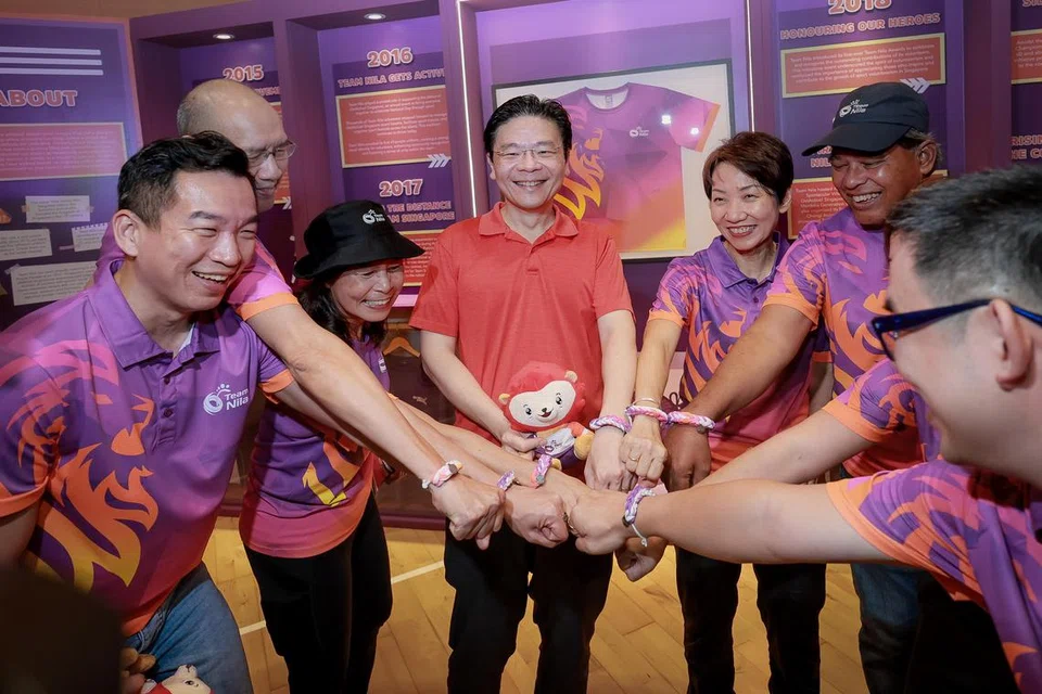 Perdana Menteri, Encik Lawrence Wong (tengah), memakai gelang persahabatan yang diperbuat daripada baju seragam Team Nila yang tidak lagi digunakan pada Karnival Team Nila di Pusat Sukan Bukit Canberra pada 8 Mac 2025. Beliau turut ditemani Setiausaha Parlimen Kanan (Kebudayaan, Masyarakat dan Belia merangkap Pembangunan Sosial dan Keluarga), Encik Eric Chua (kiri); Menteri Kemampanan dan Sekitaran, Cik Grace Fu (tiga dari kanan).