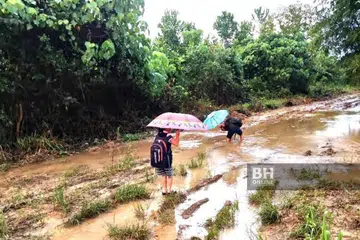 RUTIN PERIT: Darren Dinis dan adiknya Sheryl terpaksa meredah jalan berlumpur hingga kaki mereka berkudis untuk ke sekolah. Keperitan itu perkara rutin bagi penduduk Kampung Tampakahu, 28 km dari Pitas di utara Kota Kinabalu, kerana itu saja jalan yang menghubungkan kampung mereka.