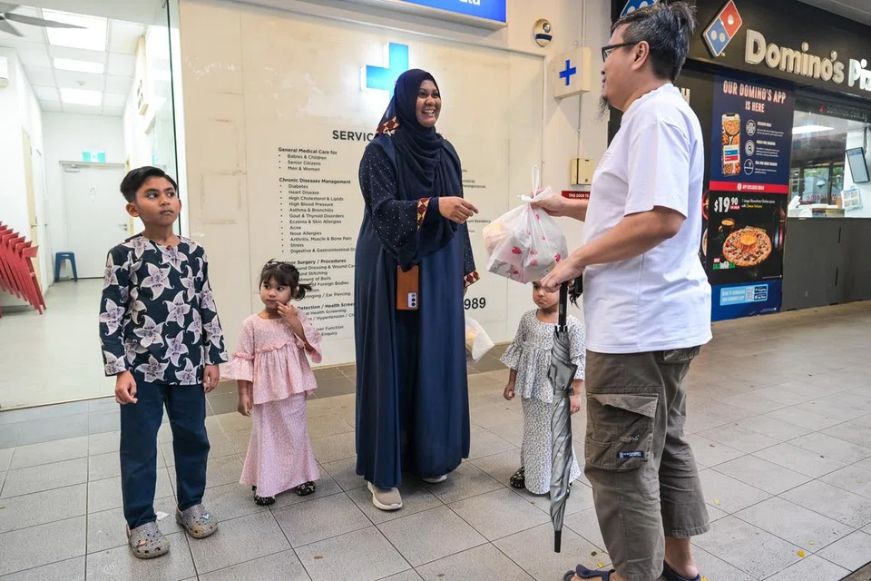 Cik Dayana Shahirah Ridwan, ditemani tiga anaknya, memberikan bungkusan makanan kepada seorang penduduk Bayview yang berada di Sumang Walk, Punggol.