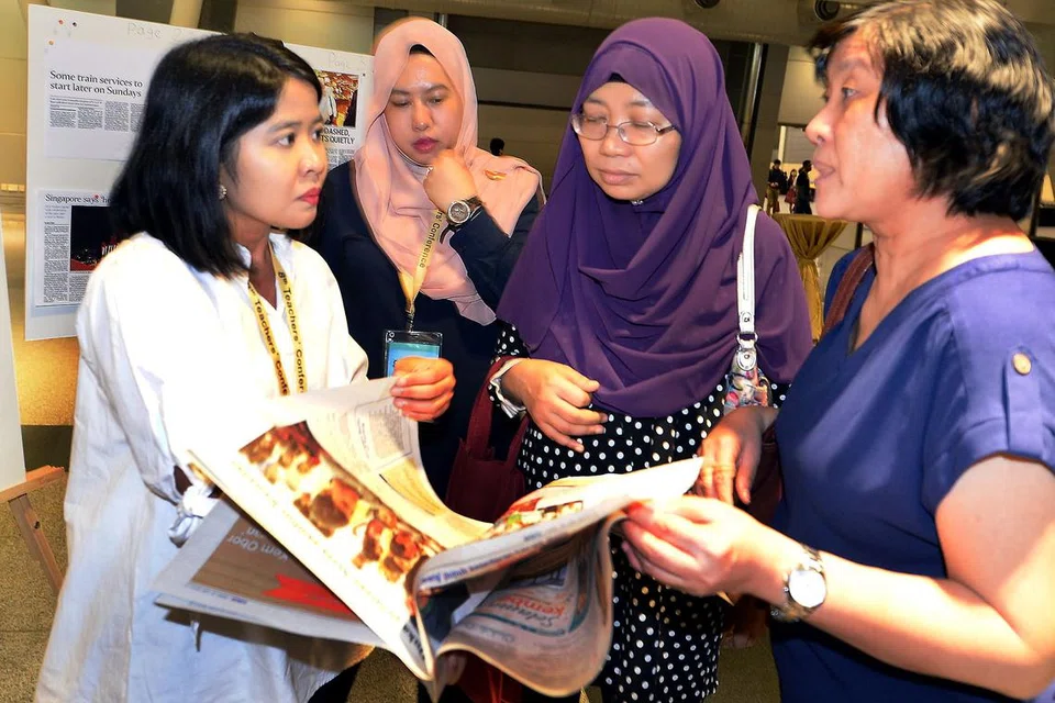 BERI PENERANGAN: Wartawan Berita Harian, Cik Ervina Mohamed Jamil (kiri), dan wartawan grafik, Cik Nur Amanina Ismail (dua dari kiri), memberi penerangan kepada peserta di reruai BH dalam Persidangan Guru di Singapore Expo semalam. - Foto ZAINAL YAHYA