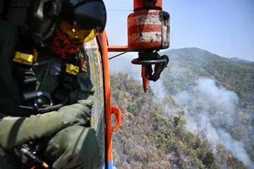 Seorang anggota Jabatan Pencegahan dan Pengurusan Bencana Thailand (DDPM) memeriksa titik-titik kebakaran dari sebuah helikopter pemadam kebakaran sebelum menjatuhkan air bagi memadamkan kebakaran hutan di daerah Mae On, wilayah utara Chiang Mai pada 26 Mac 2025. Kebakaran hutan sedang berlaku di beberapa kawasan di utara Thailand, menyumbang kepada lonjakan tahunan pencemaran udara yang turut dipacu oleh amalan pembakaran jerami oleh petani bagi menyediakan tanah untuk musim tanaman seterusnya.