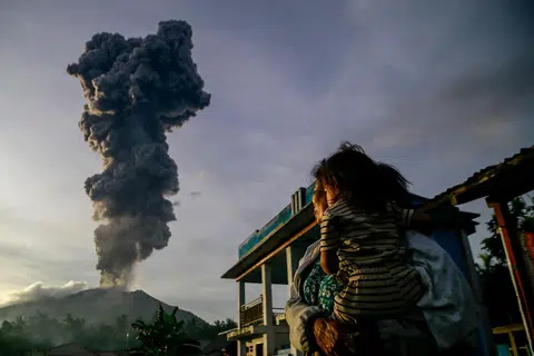 Seorang wanita dan kanak-kanak memerhatikan abu gunung berapi yang naik ke udara semasa letusan Gunung Ibu, seperti yang dilihat dari Kampung Duono di Halmahera Barat, Provinsi Maluku Utara, pada 15 Januari.