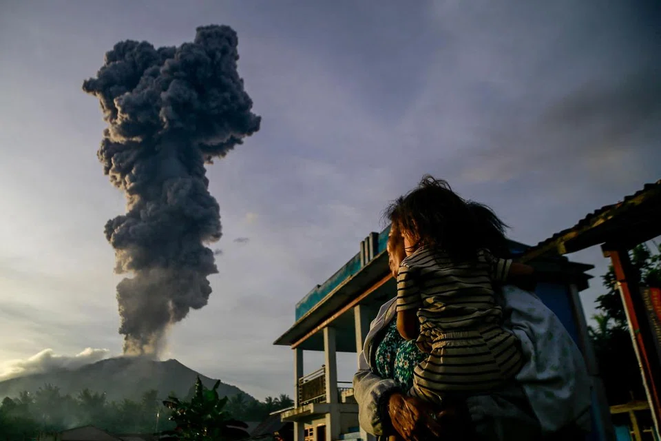 Seorang wanita dan kanak-kanak memerhatikan abu gunung berapi yang naik ke udara semasa letusan Gunung Ibu, seperti yang dilihat dari Kampung Duono di Halmahera Barat, Provinsi Maluku Utara, pada 15 Januari.