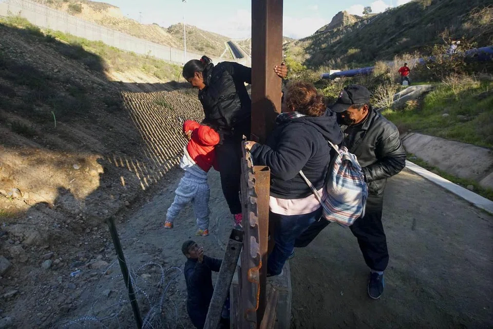 PUNCA ISU: Pagar dawai di sempadan Amerika-Mexico di Sungai Tijuana di negeri Baja California. Presiden Trump mahu membina tembok konkrit bagi menghalang pendatang haram, seperti rakyat Hondura ini (atas), yang memanjat pagar di sempadan itu pada 6 Januari lalu ini untuk memasuki Amerika. - Foto AFP