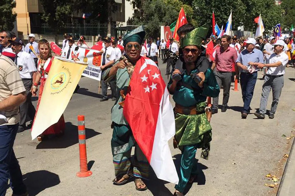BANGGA DAPAT TONJOLKAN BUDAYA SINGAPURA: Penulis (kiri) dan Encik Mohammad Alfyan Ariff Bahari, pengasas Traditional Archers Singapore, yang mengencang anaknya, berarak dengan mengenakan baju Melayu siap dengan kain samping, tanjak dan keris di bandar Marash bersama peserta dari seluruh dunia. - Foto ihsan USTAZ FACHRUDDIN DZAKI MOHAMED