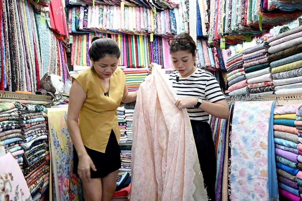 Cik Vuong Thi Bich Dao atau lebih mesra dengan panggilan Cik Sakura (kiri) membantu wartawan Berita Minggu, Cik Dahlia Zulkifli, memilih kain jenis kapas sulam untuk dibuat baju kurung. Baju kurung ditempah itu berharga $180. 