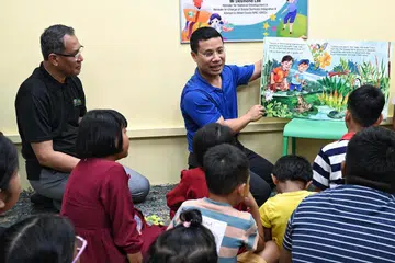 Encik Desmond Lee (memegang buku) membacakan buku kepada kanak-kanak pelbagai kaum dan latar belakang semasa sesi bercerita pada pelancaran perpustakaan mini di Jampacked@West Coast pada 21 April.