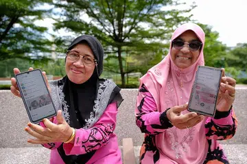 SUDAH TIDAK TERKIAL-KIAL: Cik Asmah Talib, 64 tahun (kiri) dan temannya Cik Salmabee Abdul Kadir, 66 tahun, yang telah menghadiri bengkel celik digital warga emas Jom Surf! Januari lalu, menunjukkan aplikasi HealthHub dan SingPass dalam telefon bimbit mereka. - Foto BM oleh THADDEUS ANG