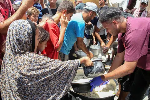 Penduduk Palestin berasak-asak bagi mendapatkan makanan yang diagihkan oleh, Cef Hamada Shaqoura (kanan), di Khan Younis, di selatan Jaluran Gaza pada 22 Ogos. 