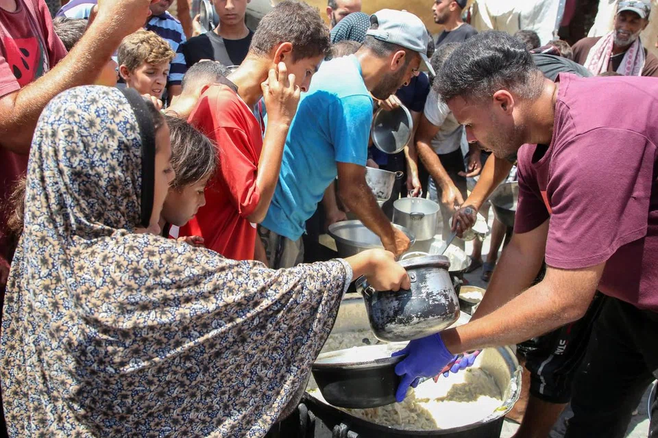 Penduduk Palestin berasak-asak bagi mendapatkan makanan yang diagihkan oleh, Cef Hamada Shaqoura (kanan), di Khan Younis, di selatan Jaluran Gaza pada 22 Ogos. 
