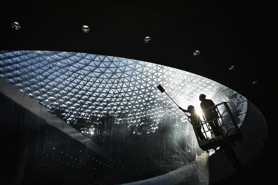 PEMBERSIHAN BAHAGIAN LUAR: Pekerja membersihkan bahagian luar ruangan yang diperbuat daripada akrilik yang merentangi lantai bawah tanah satu dan dua air terjun HSBC Rain Vortex di Jewel, Lapangan Terbang Changi. - Foto-foto BH oleh ARIFFIN JAMAR