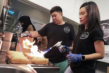 GIGIH PERBAIKI KHIDMAT DALAM TALIAN: Ikah Jamil (kanan) dan rakan niaganya, Aliff Zainal, mengubah suai perniagaan dalam talian 'hot dog' dan minuman di dapur pusat yang baru diperolehi sekitar Centropod, Changi Road, apabila Bazar Raya ditiadakan tahun ini. - Foto BH oleh MARCELLIN LOPEZ