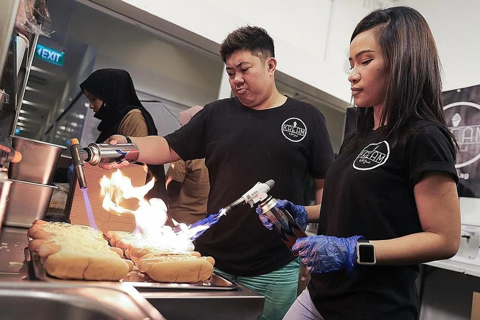 GIGIH PERBAIKI KHIDMAT DALAM TALIAN: Ikah Jamil (kanan) dan rakan niaganya, Aliff Zainal, mengubah suai perniagaan dalam talian 'hot dog' dan minuman di dapur pusat yang baru diperolehi sekitar Centropod, Changi Road, apabila Bazar Raya ditiadakan tahun ini. - Foto BH oleh MARCELLIN LOPEZ
