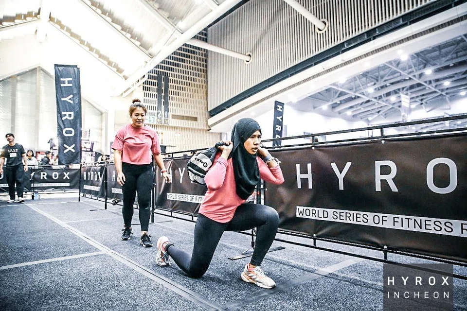 Cik Nurulain Wahab melakukan senaman ‘lunge’ atau gerak maju sambil mengangkat beg pasir bagi salah satu stesen Hyrox di Korea.