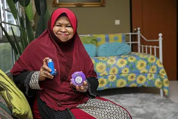 LINDUNG DARIPADA COVID-19: Ustazah Aslinda, yang telah mendapatkan dos pertama vaksinasi Covid-19, bersama ubat semputnya. Kini beliau lebih yakin dapat melindungi diri dan muridnya daripada Covid-19. - Foto BH oleh YONG LI XUAN