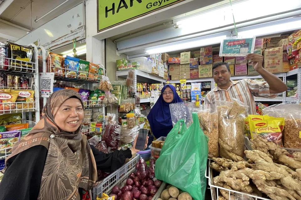 BELI KEPERLUAN DAPUR: Cik Siti Hanifa Ahmudon (kiri) membeli barang keperluan dapur di gerai milik Encik Haron Amat (kanan) dan isteri, Cik Riry Fitria Maricar (tengah), menggunakan baucar CDC.
