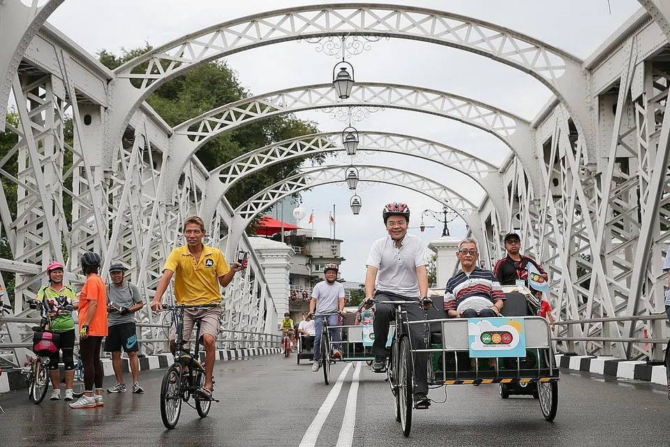 SUASANA MERIAH MESKI HUJAN: Suasana di kawasan sivik Singapura semalam sempena acara Ahad Bebas Kereta SG yang memperlihatkan Menteri Pembangunan Negara, Encik Lawrence Wong, mengayuh beca yang ditumpangi seorang warga emas (kanan). Pada acara kali ini lebih banyak jalan raya ditutup dan hanya boleh dilalui kenderaan ringan seperti basikal dan beca demi membolehkan orang ramai menggunakan jalan raya dengan lebih santai. - Foto THE STRAITS TIMES