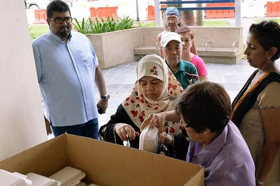 SEMANGAT MEMBANTU YANG KUAT: Encik Nizar Mohd Shariff (kiri) melihat bungkusan makanan yang diedarkan kepada golongan susah di kolong sebuah blok flat di Marine Terrace baru-baru ini. - Foto KHALID BABA
