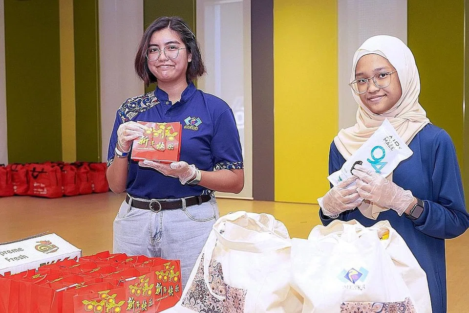 HARGAI WIRA: Cik Siti Sarah Annuar (kiri) dan Cik Umairah Hanisah Normanshah gembira dapat meluangkan masa melahirkan penghargaan kepada pekerja barisan hadapan seperti penghantar makanan dan pekerja pembersihan dengan mengedarkan beg penjagaan di Our Tampines Hub semalam.