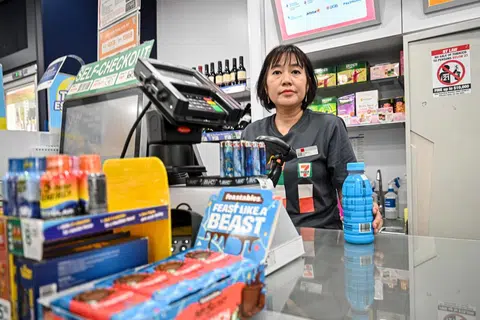 Seorang jurujual yang bertugas di kedai runcit, 7-Eleven mengurus kaunter wang dan memberi perkhidmatan pelanggan yang cekap dan mesra.