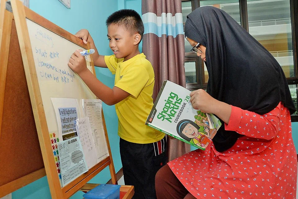 DAHAGAKAN ILMU: Muhammad Aniq Irfan gemar membaca dan belajar walaupun huruf yang dibacanya kadangkala nampak terbalik pada pandangannya disebabkan disleksia. Menulis juga memerlukan perhatian dan tumpuan kerana jika tidak, tulisannya itu tidak kemas dan huruf yang ditulisnya boleh berbolak-balik. Ibunya, yang hanya mahu dikenali sebagai Cik Sarah (kanan), amat memahami keadaan anaknya itu dan mencuba sebaik mungkin untuk membantu. - Foto JOHARI RAHMAT