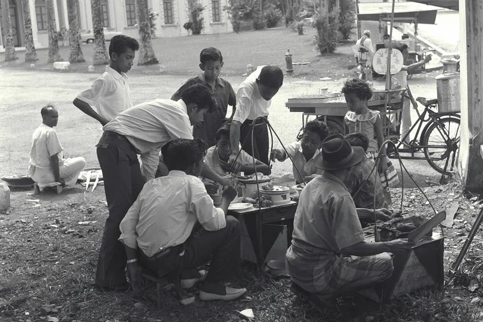 Sekumpulan pemuda menjamu selera dengan sate yang dibeli daripada pegerai jalanan pada 1 Syawal. Gambar ini diambil Mac 1962.
