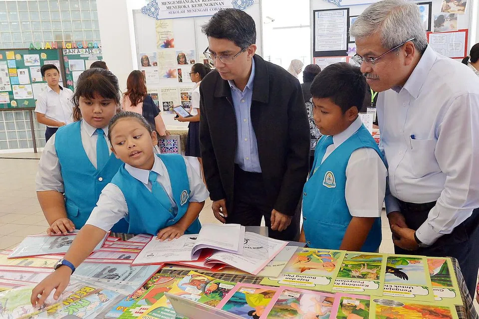 GERAI ILMU: Murid Sekolah Rendah Park View (dari kiri) Elina Norhisham, Siti Zahra Fahrudin dan Muhammad Izz Matiin Yakob menunjukkan bahan pembelajaran kepada Dr Muhammad Faishal Ibrahim (jaket hitam) yang ditemani Pengarah MLCS, Encik Mohd Noh Daipi (kanan) dalam 'Seminar Bahasa Melayu 2016', semalam. - Foto TUKIMAN WARJI