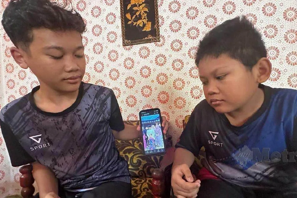 Muhammad Haziq Muhammad Karim, 15 tahun (kiri) dan adiknya, Syahmi, 13, menunjukkan gambar arwah kakaknya, Manarina Hasya.