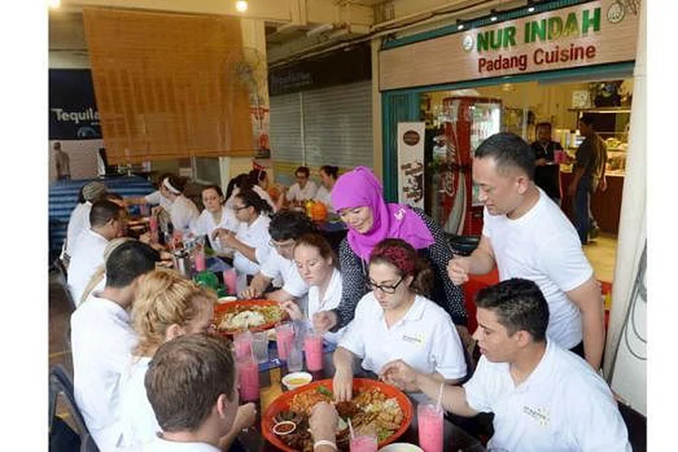 KONGSI BUDAYA: Hajah Roziah Adon, sambil diperhatikan Encik Dean Yassin, sedang menjelaskan kepada pelajar sekolah kulinari terbaik di Amerika Syarikat, Universiti Johnson and Wales, bagaimana menikmati nasi ambeng - sebagai sebahagian daripada program mengenali budaya dan masakan Asia. - Foto TAUFIK A. KADER