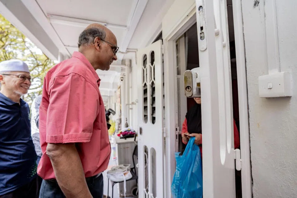 DEKATI MASYARAKAT: Bekas menteri kanan, Encik Tharman Shanmugaratnam (tengah), mengagihkan pek bantuan merangkumi daging korban, nasi mandi dan baucer pasar raya Sheng Siong kepada penduduk di Mei Ling Street. 