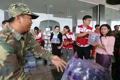 HULUR BANTUAN: Pasukan Palang Merah Singapura yang memakai jaket merah (dari kiri) Cik Jacqueline Ng, Cik Geraldine Aggarao dan Encik Samuel Lee membantu menyusun bekalan yang dibawa mereka termasuk air botol, mi segera, makanan dalam tin dan sebagainya. - Foto-foto BH oleh JONATHAN CHOO KK 