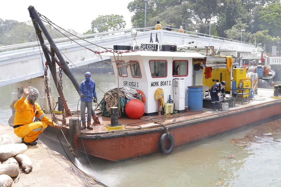 TIGA BOT DIKERAHKAN: Seramai 15 pekerja daripada Singapore Oil Spill Response Centre Pte Ltd giat membersihkan pencemaran minyak di kawasan Terminal Feri Changi Point, semalam. - Foto FARAH REZAL