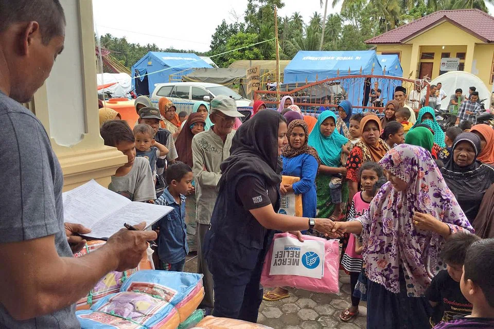AGIH BANTUAN: Pengurus program bagi Program Antarabangsa Mercy Relief; Cik Saleha Ali (berbaju hitam), sedang bersalaman dan membahagikan pek bantuan keperluan asas kepada seorang penduduk Aceh yang terjejas dengan gempa bumi bulan lalu. - Foto MERCY RELIEF