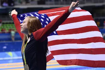 EMAS BERMAKNA: Perenang Amerika, Lilly King, mengibarkan bendera negaranya di podium pemenang selepas mengatasi pesaingnya dari Russia yang pernah gagal ujian dadah sebelum ini, Yulia Efimova, di final perlumbaan 100 meter kuak dada wanita di temasya Sukan Olimpik ini kelmarin. - Foto AFP