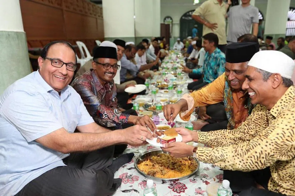 ERATKAN JALINAN: Menteri Perhubungan dan Penerangan, Encik S. Iswaran (kiri ) dan pengerusi Masjid Jamae Chulia, Encik Shaick Fakrudeen S Ali (di kirinya), mengambil kurma yang dihulurkan pegawai masjid dalam majlis berbuka puasa yang turut disertai seramai 1,400 jemaah di masjid itu Sabtu lalu. - Foto FACEBOOK S. ISWARAN