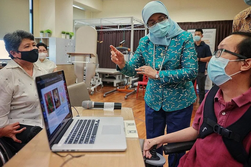 DEKATI MASYARAKAT: Presiden Halimah Yacob melihat rekaan kad oleh Encik Timothy Chan, 31 tahun, sewaktu lawatan beliau ke MDAS semalam. Bersama beliau ialah Pengarah Eksekutif MDAS, Cik Judy Wee (kiri). - Foto BH oleh JASON QUAH