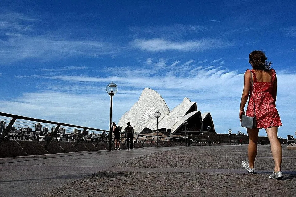 LENGANG: Seorang wanita kelihatan berjalan di kawasan sekitar Sydney Opera House yang lengang. Kawasan tarikan ini lazimnya dibanjiri pengunjung and pelancong dari luar negara. - Foto AFP