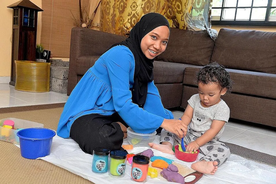 BUAT DOH MAINAN: Cik Siti Nuratiqah menunjukkan anaknya Muhammad Uwais Haq Mohd Iqbal cara bermain dengan doh mainan yang dibuatnya sendiri. - Foto BM oleh NUR DHUHA ESOOF