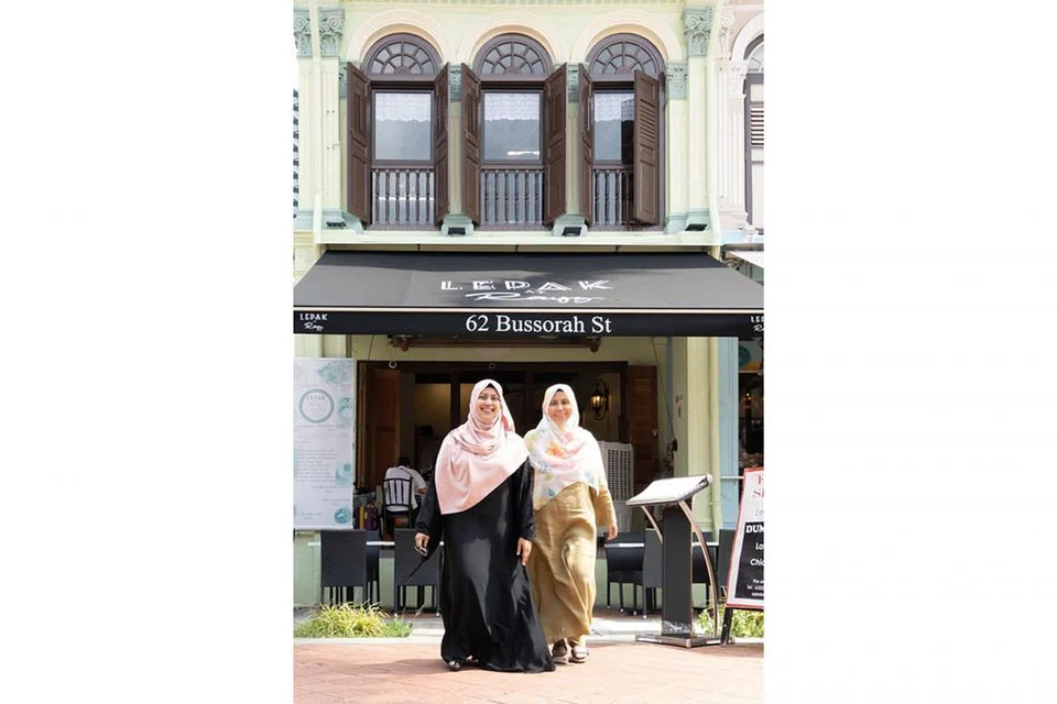 INGIN KEMBALIKAN PERISA JUADAH KAMPUNG: Cik Aziah (kiri) dan Cik Nor Aishah Abu Samah, isteri Encik Rosman, akan menyiapkan juadah tradisional, termasuk kuih talam yang popular di Kampung Khaji dahulu, untuk rumah terbuka di Taman Warisan Melayu malam ini. - Foto TWM