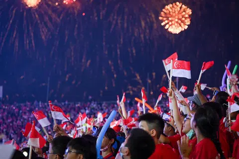 BANGGA JADI RAKYAT SINGAPURA: Para pelajar yang hadir pada pertunjukkan NE melambaikan bendera Singapura sambil menyaksikan persembahan bunga api yang mewarnai kawasan di sekitar Padang. 