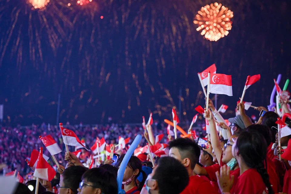BANGGA JADI RAKYAT SINGAPURA: Para pelajar yang hadir pada pertunjukkan NE melambaikan bendera Singapura sambil menyaksikan persembahan bunga api yang mewarnai kawasan di sekitar Padang. 