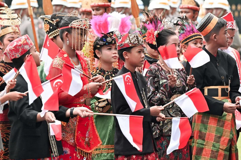 Para pelajar mengibarkan bendera Singapura sebagai menyambut ketibaan Perdana Menteri Lawrence Wong di Istana Merdeka di Jakarta pada 6 November.  