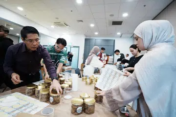 Menteri di Pejabat Perdana Menteri, Dr Mohamad Maliki Osman, yang juga Menteri Kedua (Ehwal Luar merangkap Pendidikan) (kiri) menggembleng tenaga menyiapkan kuih-muih bersama Cik Nuwairah Adriana Khairul Rizal, relawan dari badan tidak mengaut untung, Membina Community, untuk diberi sebagai cenderahati di Bazar Geylang Serai mulai 6 Mac. 