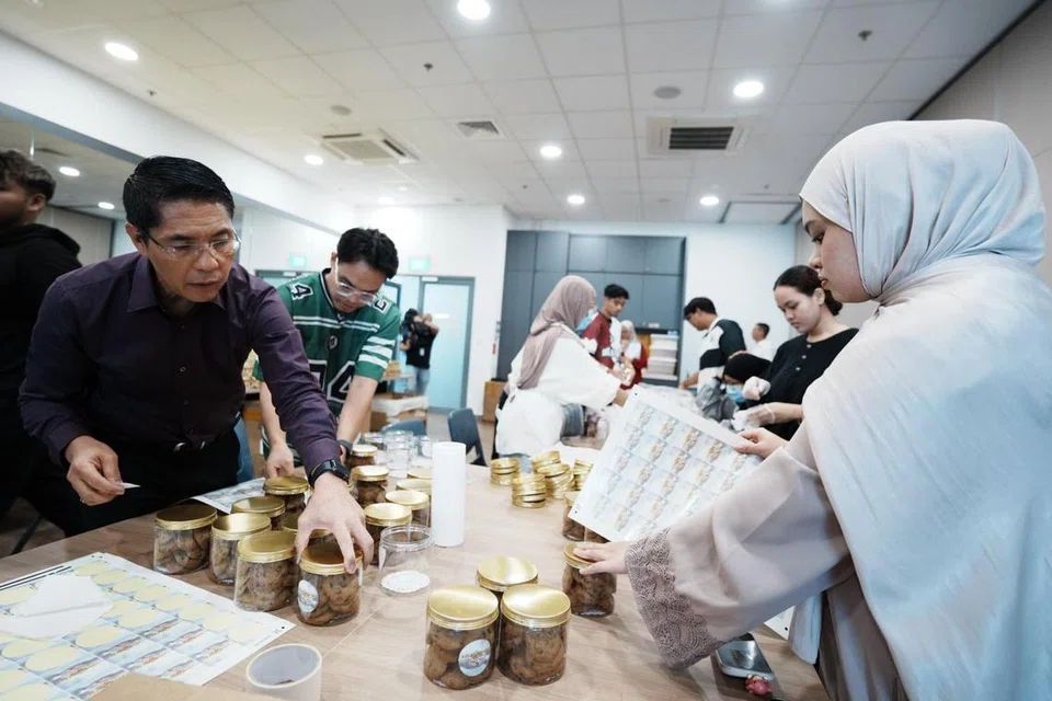 Menteri di Pejabat Perdana Menteri, Dr Mohamad Maliki Osman, yang juga Menteri Kedua (Ehwal Luar merangkap Pendidikan) (kiri) menggembleng tenaga menyiapkan kuih-muih bersama Cik Nuwairah Adriana Khairul Rizal, relawan dari badan tidak mengaut untung, Membina Community, untuk diberi sebagai cenderahati di Bazar Geylang Serai mulai 6 Mac. 