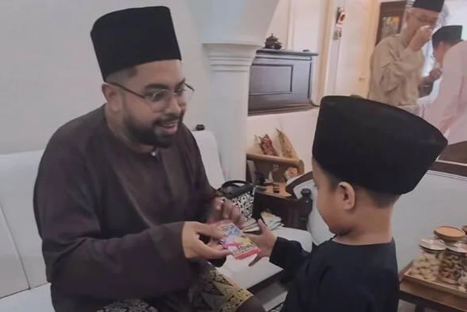 Encik Muhammad Zharfan Mohd (kiri) memberikan pek kad Pokemon sebagai duit raya kepada kanak-kanak.